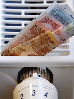 Ausschnitt Heizkörper mit Thermostat, in den Heizrippen klemmen Eurogeldscheine
